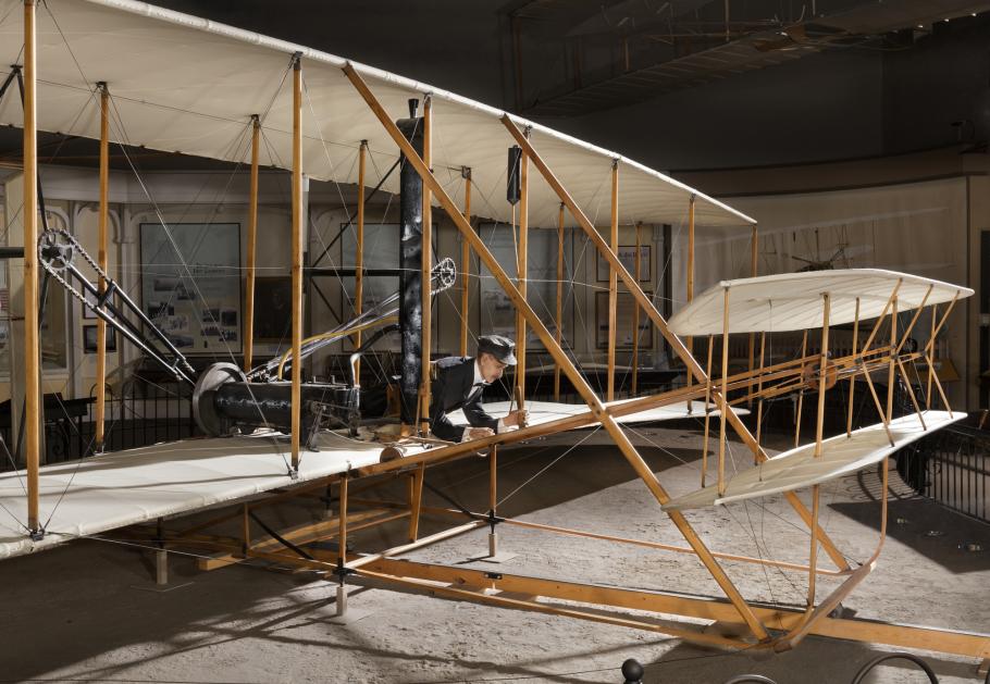 Front of 1903 Wright Flyer with model of Wright Brother laying flat in aricraft