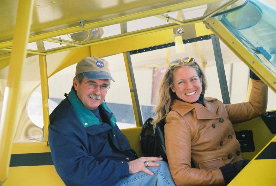 John and Heather Penney sitting in the cockpit of a yellow plane. 