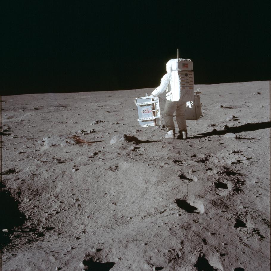 Aldrin photographed from behind on the Moon carrying equipment. 