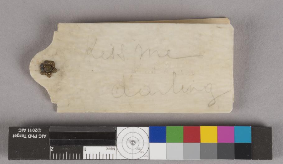 A photograph of the ivory dance card with the inscription “Kiss me darling.”