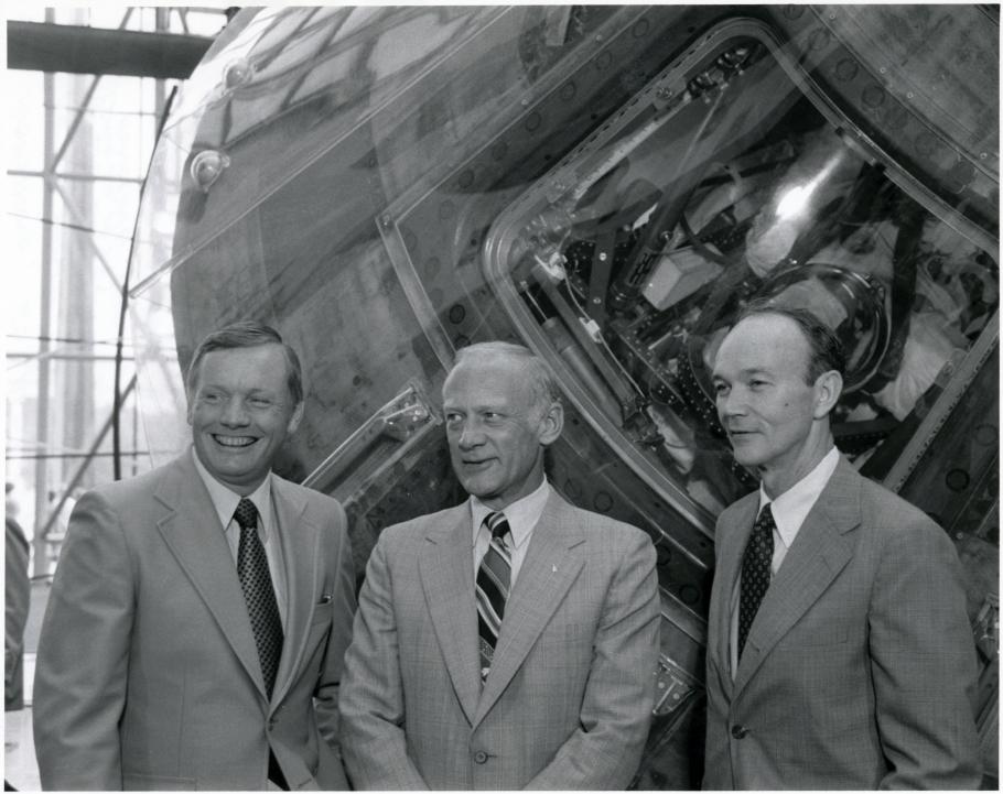 Black and white of Armstrong, Aldrin, and Collins stand beside the Apollo 11 command module.
