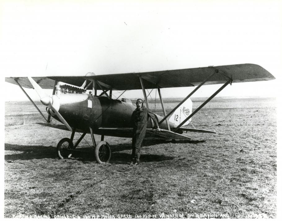 Black and white photograph of airplane with pilot in front.