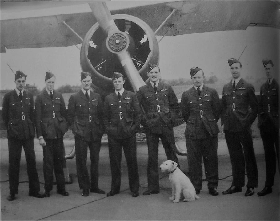 Eight airmen in front of aircraft with dog