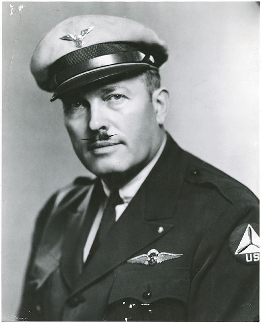 Half length black and white photograph of man, wearing a full-brim light-colored wheel hat with winged insignia and uniform with "RT" insignia wings over breast pocket. He has a mustache with pointed tips.