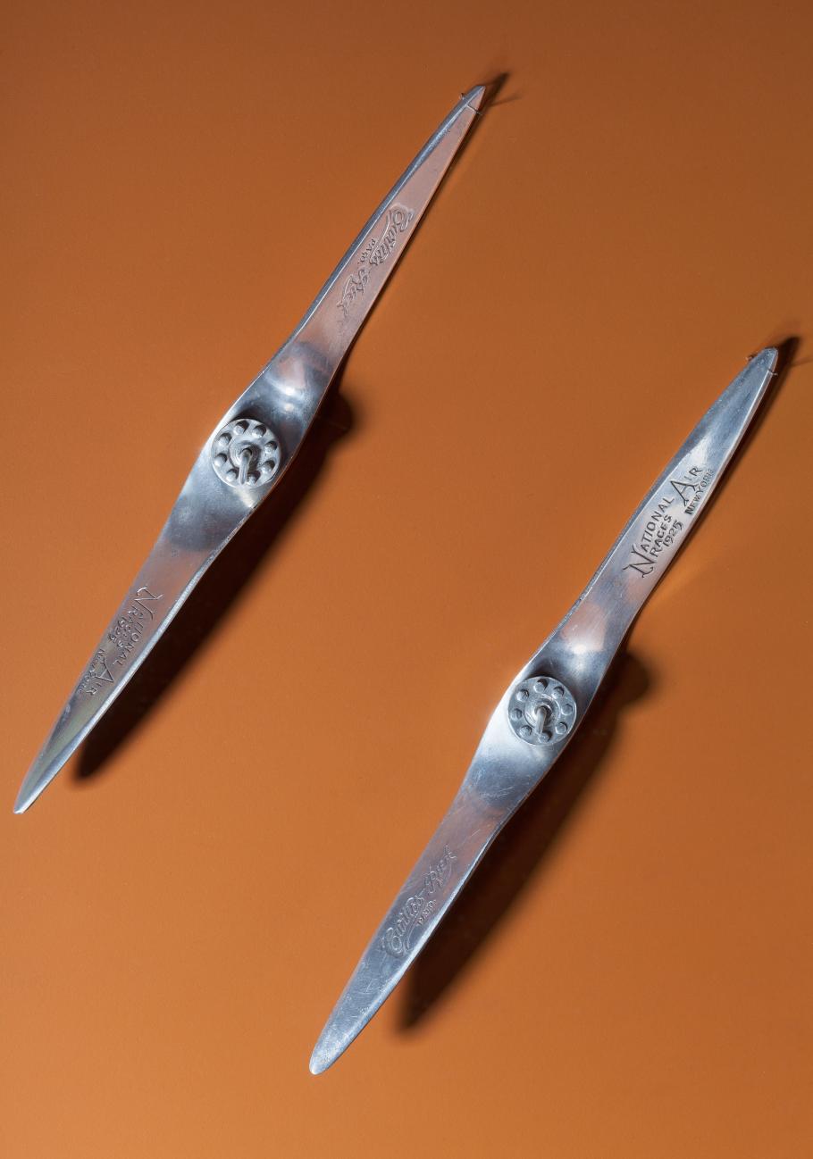 Two metal miniature propellers against an orange-red backdrop. 
