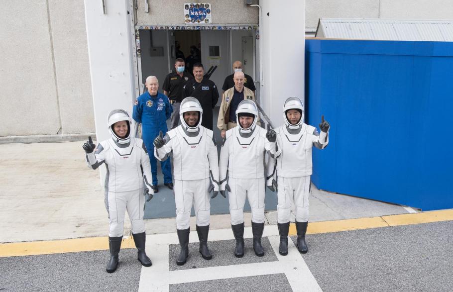 The crew of SpaceX Crew-1 stands in white spacesuits outside of the Neil A. Armstrong Operations and Checkout Building