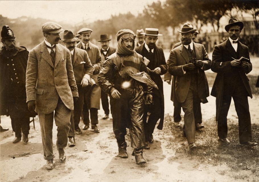 Black and white of Jules Vedrines wrapped in a leather flying suit and surrounded by others.