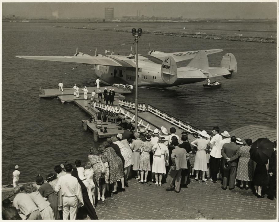 people lined up near floating dock; flying boat in water