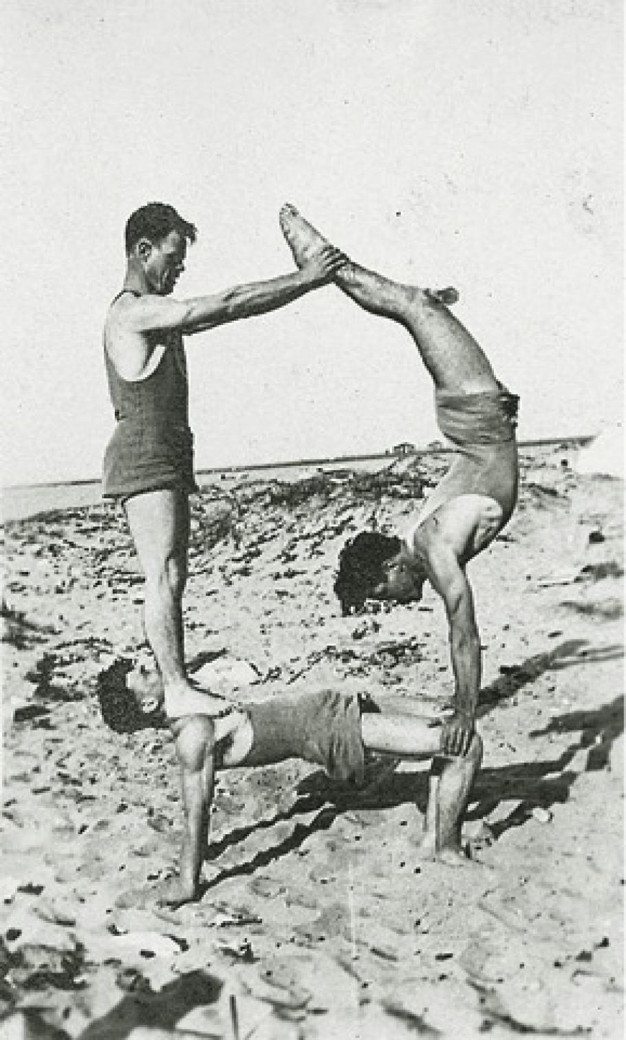 Doolittle and friends do tricks on the beach. Doolittle on the bottom holds up his other two friends who create a pyramid. 