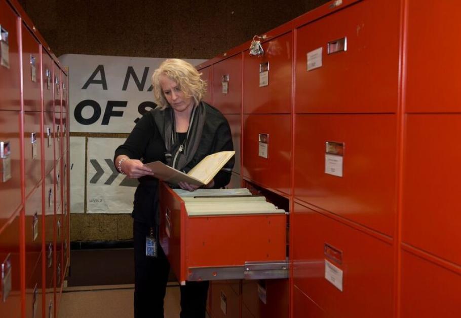 An archivist looks at a file while standing in front of a filing cabinet. 