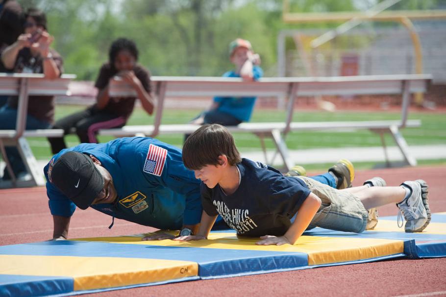 An astronaut and a student do push-ups outside. 