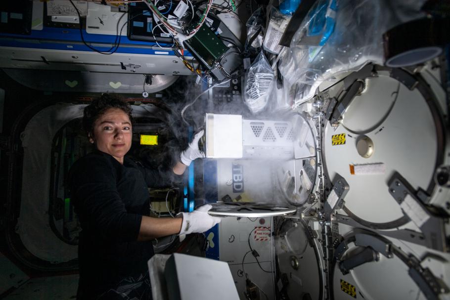 astronaut on space station retrieves samples from compartment