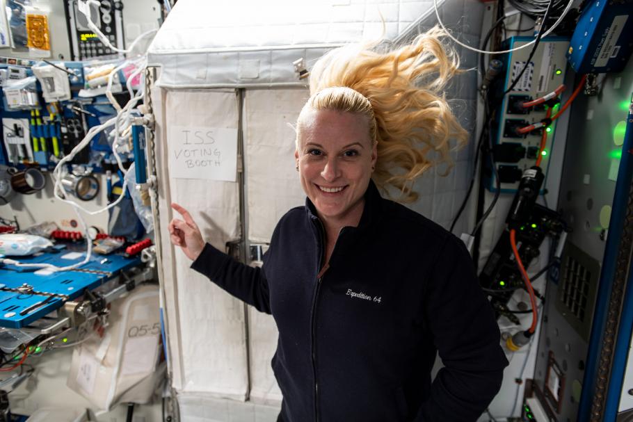 Kate Rubins in space next to sign that says ISS Voting Booth