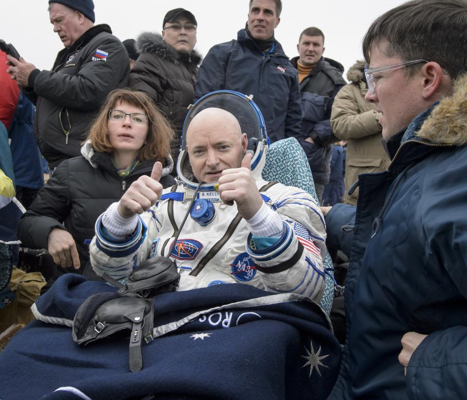 Kelly sits in his spacesuit while a crowd surrounds him. 