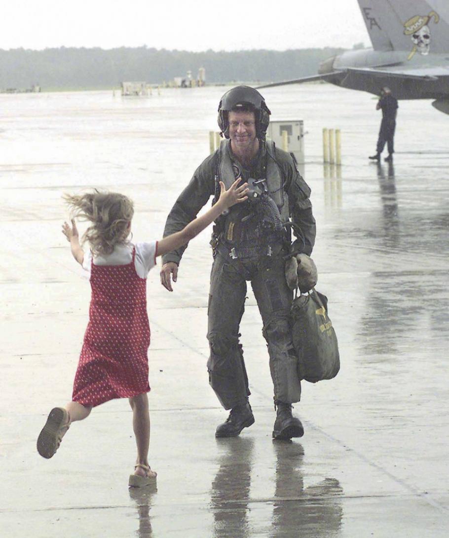A little girl runs, arms outstretched, towards a smiling man in flight gear. 