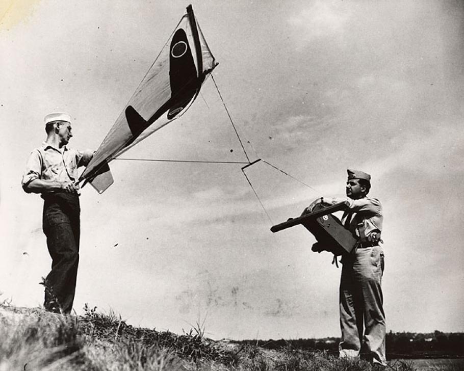 Two men hold a kite with the image of an airplane on it. 
