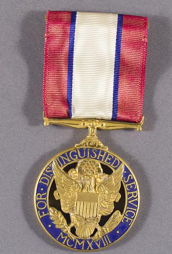 A round medal on a red, white, and blue ribbon. The medal has an eagle on it and text that reads "For Distinguished Service."