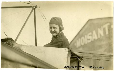 A woman smiles from the cockpit of an airplane.