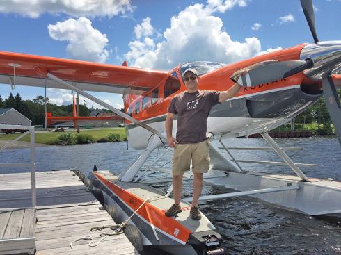 Man dressed in t-shirt and shorts standing on his floatplane on a lake