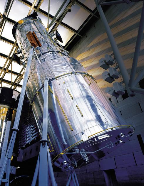 A back-up model of the Hubble Space Telescope on display in the Museum. It’s a 43-foot long cylinder covered in aluminum foil with appendances, mounted at a slight angle on a large frame.