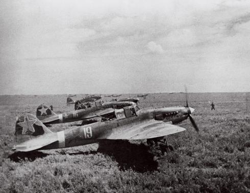 A fleet of sleek IL-2 ground attack aircraft prepare to take off from a grassy airfield, their propellers spinning.