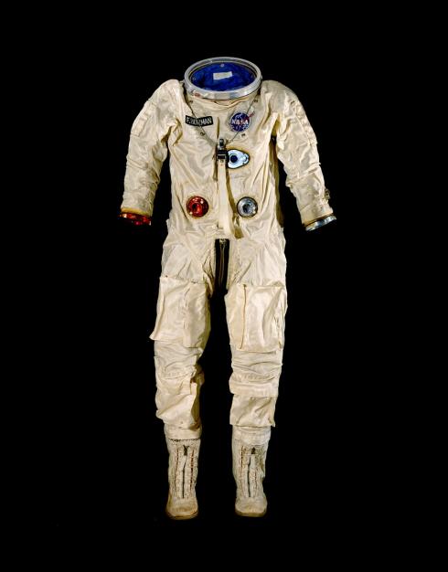 A cream colored space suit with accents of red and blue posed against a black background. There are boots attached but no helmet or gloves.