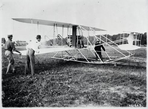 A photo of three men readying the Wright Military Flyer. Two men stand next to its wing, and the other stand between the landing skids.