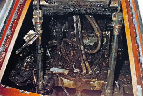 View through the hatch of the Apollo 1 space capsule after the fire showing a charred mess of wires and equipment.