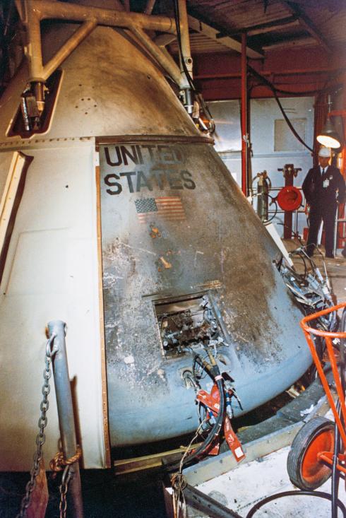 The Apollo 1 command module—its clean white and grey exterior slightly charred— sits in the white room the day after the accident.