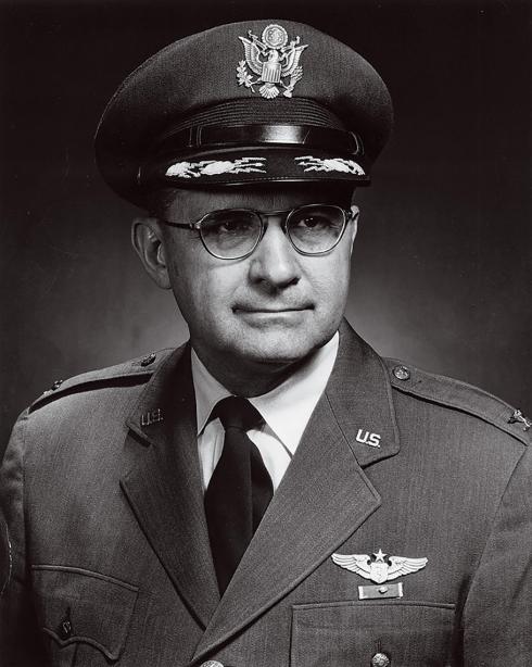 A black and white photograph of Colonel John P. Stapp, a man in a formal military uniform. He is wearing glasses.