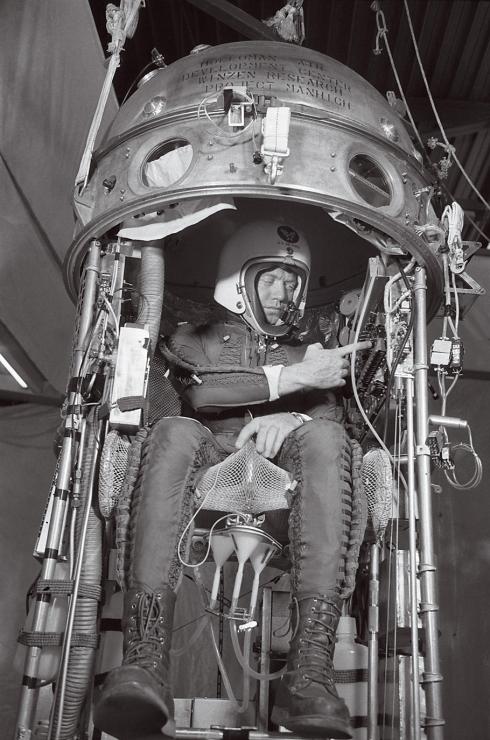 Joe Kittinger, clad in a helmet and a pressure suit, checks the scientific equipment inside his capsule-like gondola.