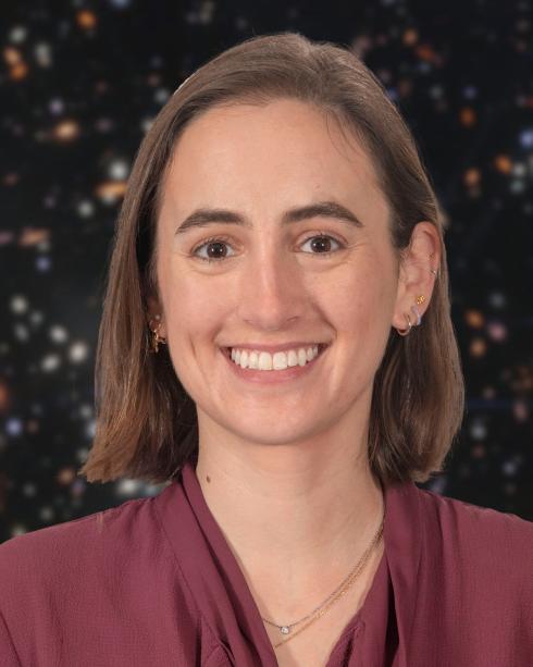 Portrait of a woman. She is smiling and wearing a burgundy shirt. Behind her is a star field.