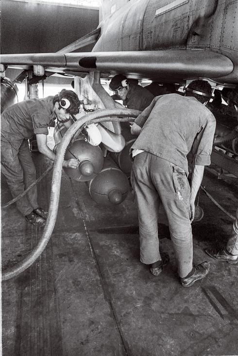 In this black and white photo, two men wearing noise-cancelling headsets are loading a missile onto an aircraft. 