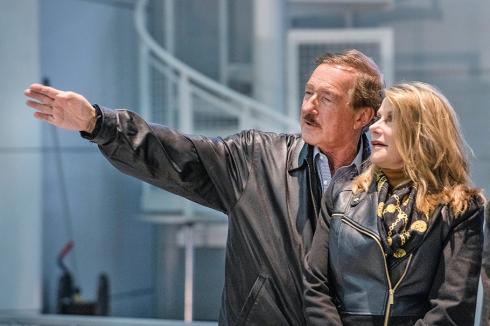 Steven F. Udvar-Hazy, a middle-aged man with dark hair and a mustache, points out an exhibit to his wife Christine, who has shoulder-length blonde hair and, like her husband, is wearing a leather jacket.