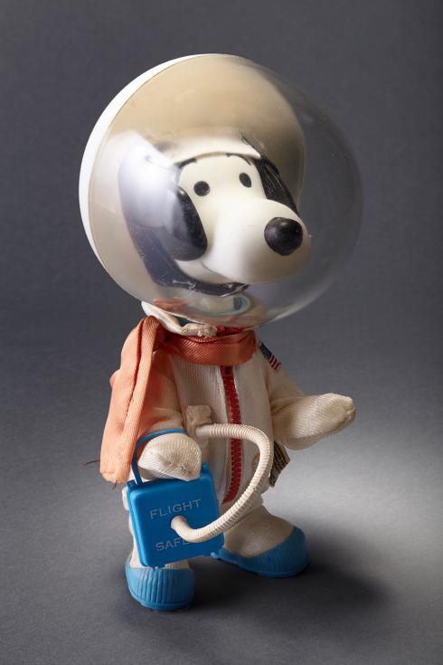 A vintage Snoopy doll, a cartoon dog, is dressed as an astronaut, wearing a comical, see-through spherical helmet.