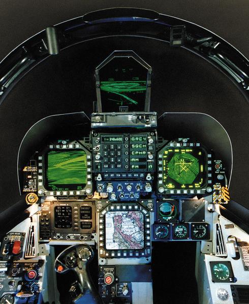 Four display panels glow green and white in the cockpit of a military jet simulator.