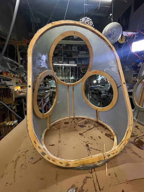 The empty upper torso of Adam Savage's spacesuit is in the early stages of construction, made from clear plastic and with plywood framing the torso and the openings for the arms, head, and waist.