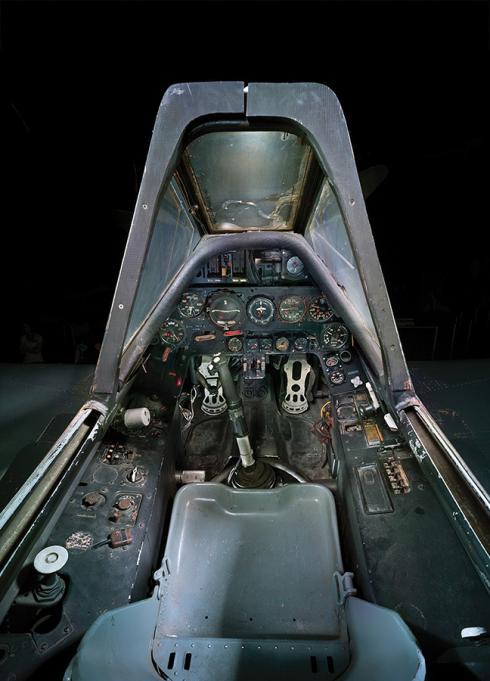 A large center stick dominates the view inside a single-seat cockpit, with control panels filled with dials and switches.