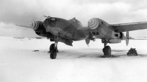 A black-and-white photo shows a World War II-era P-38G bomber parked in the frozen, empty wasteland of Alaska.