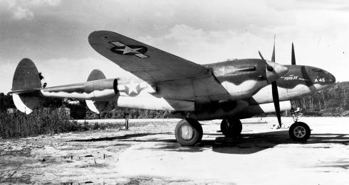 A black-and-white photo shows a World War II-era aircraft, the F-4, parked in an empty field.