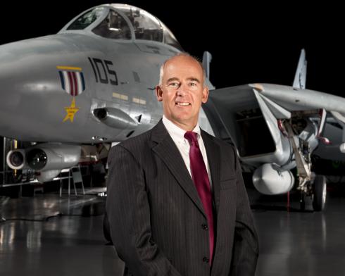 Portrait shot of a man in a suit standing in front of aircraft in a museum setting.