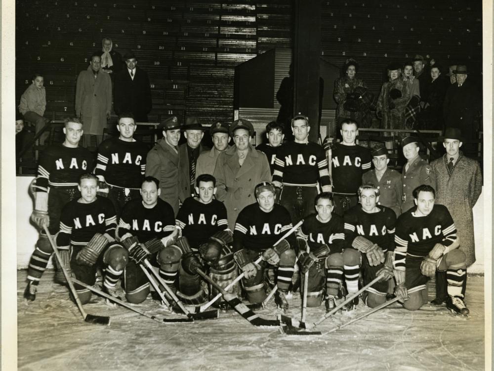 A group of men pose wearing hockey uniforms. Some of the men are holding hockey sticks.