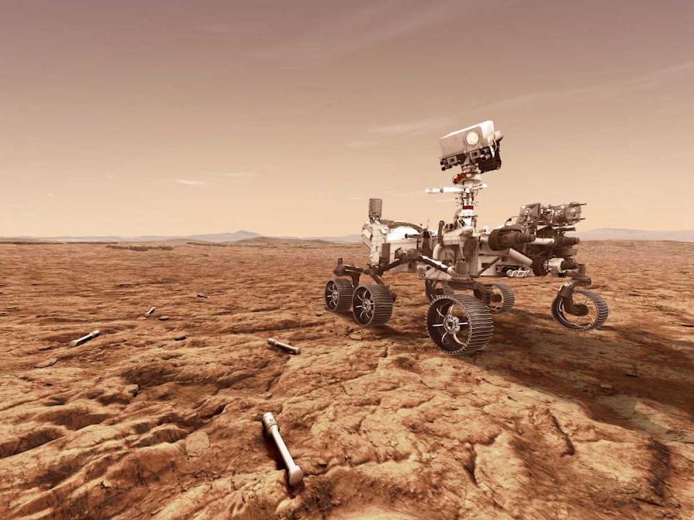 A rending of a six wheeled rover with a camera affixed to a "neck" giving it an anthropomorphized appearance. On the orange ground around the rover, there are white tubes.  