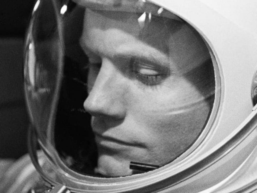 A man in a spacesuit helmet looks down. 