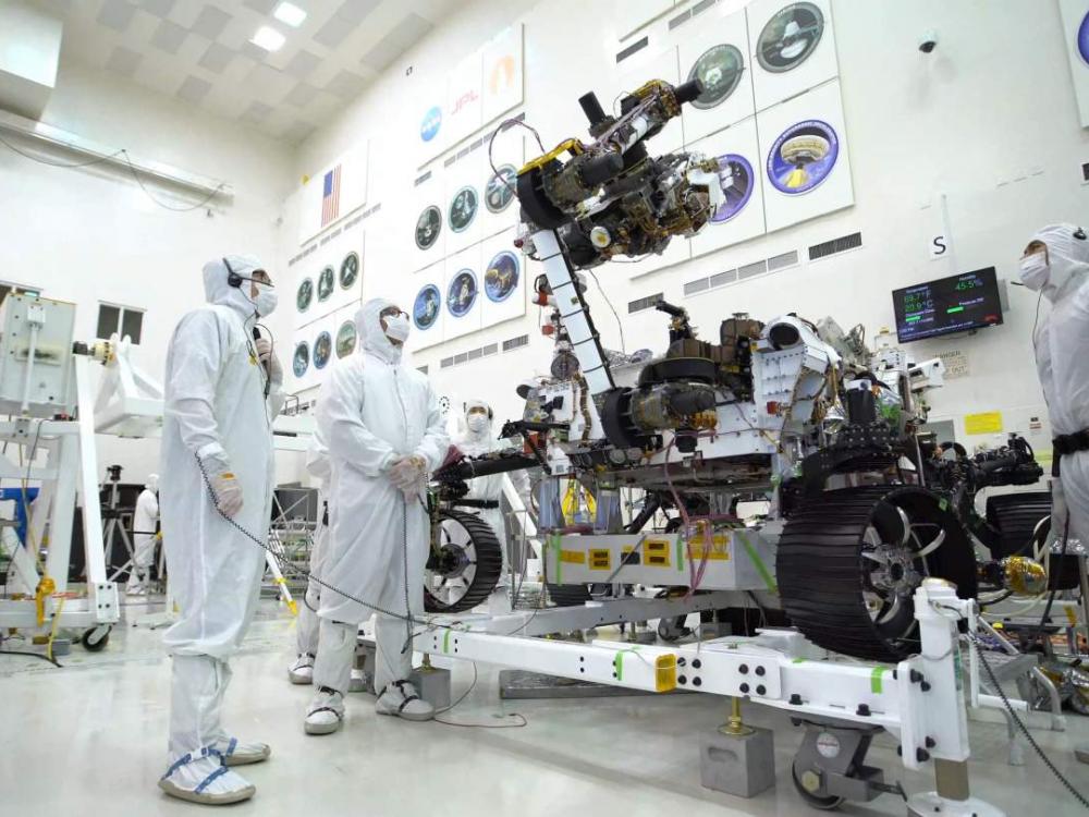 Three people in white protective suits work on rover