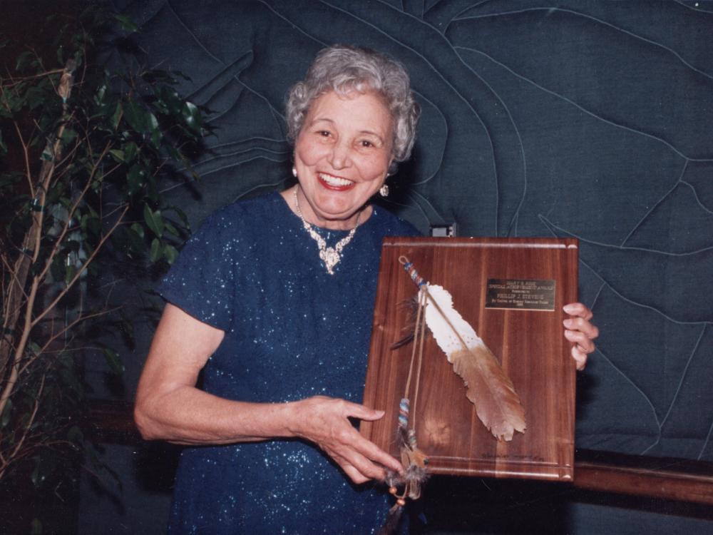 woman in blue dress holding an award plaque with a feather on it