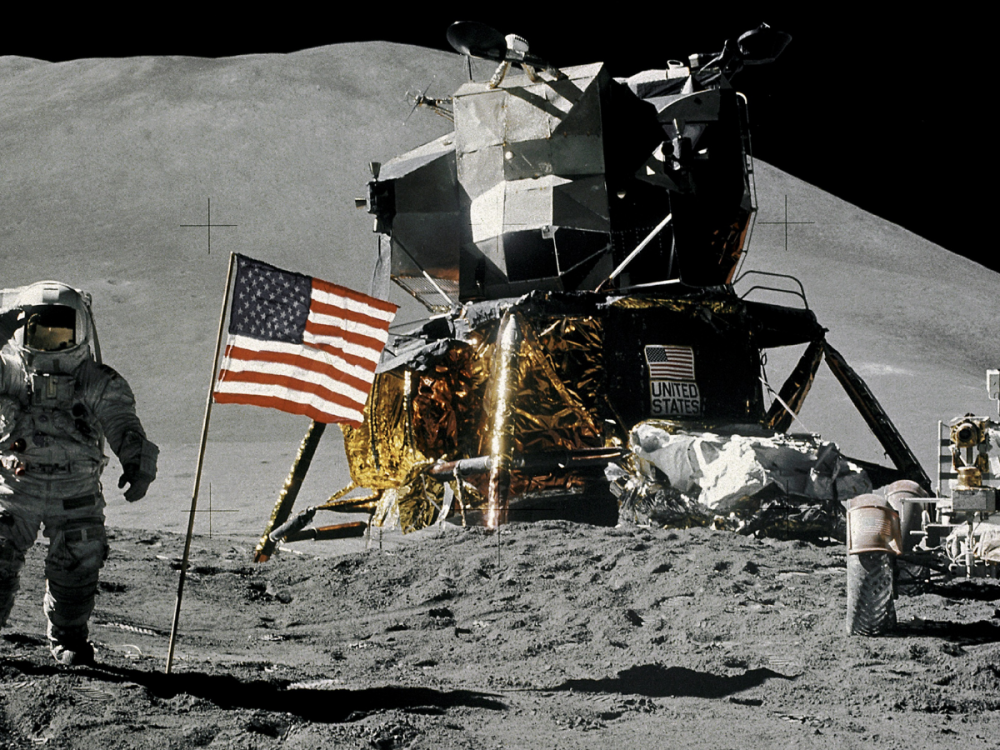astronaut on the moon next to American flag, lunar module, and lunar roving vehicle 