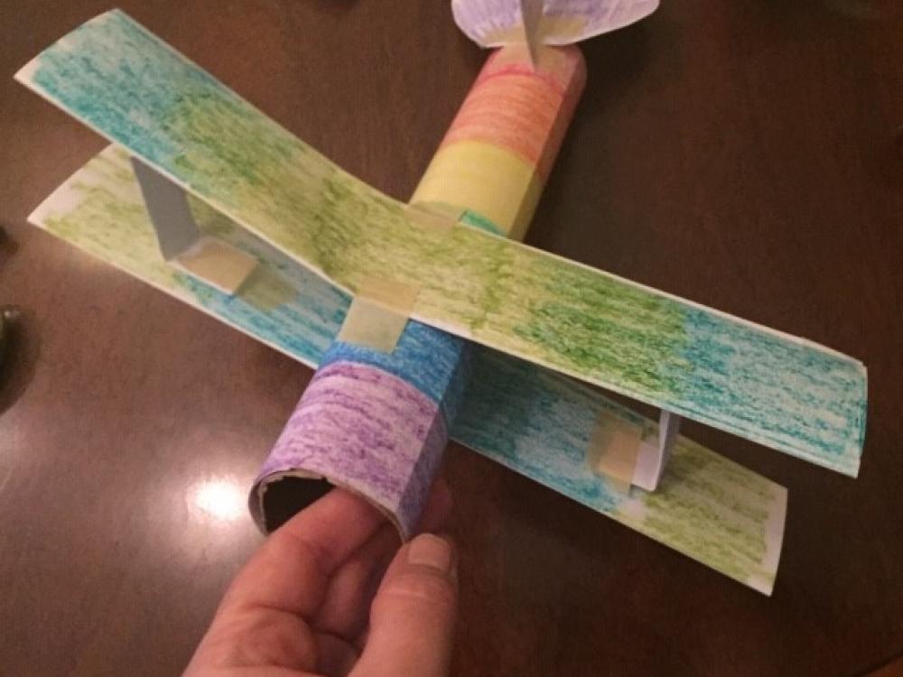 A small plane made from a paper towel roll, colored multiple colors. 