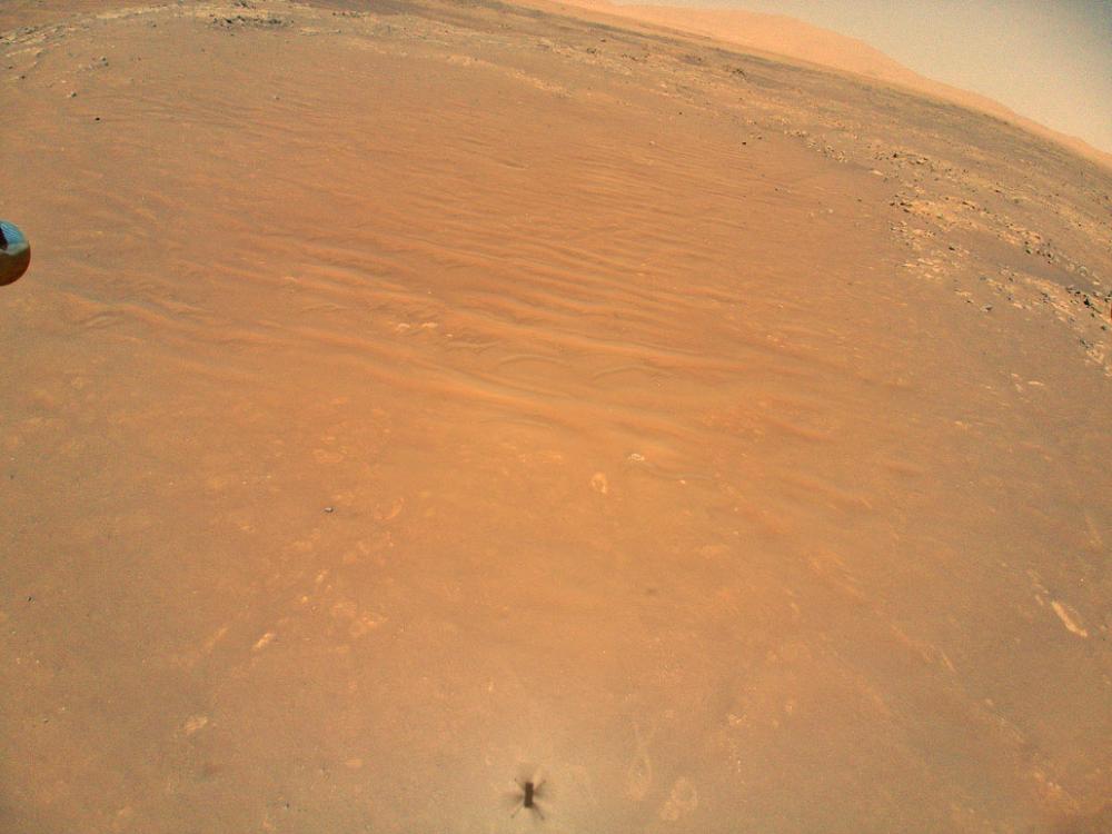 An image of the orange surface of Mars seen from the perspective of the Ingenuity helicopter.