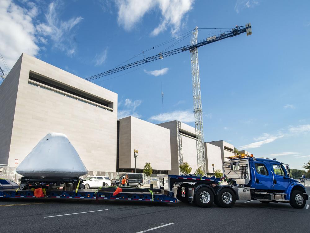 Command module Columbia at the back of a big truck with the National Air and Space Museum in the background.